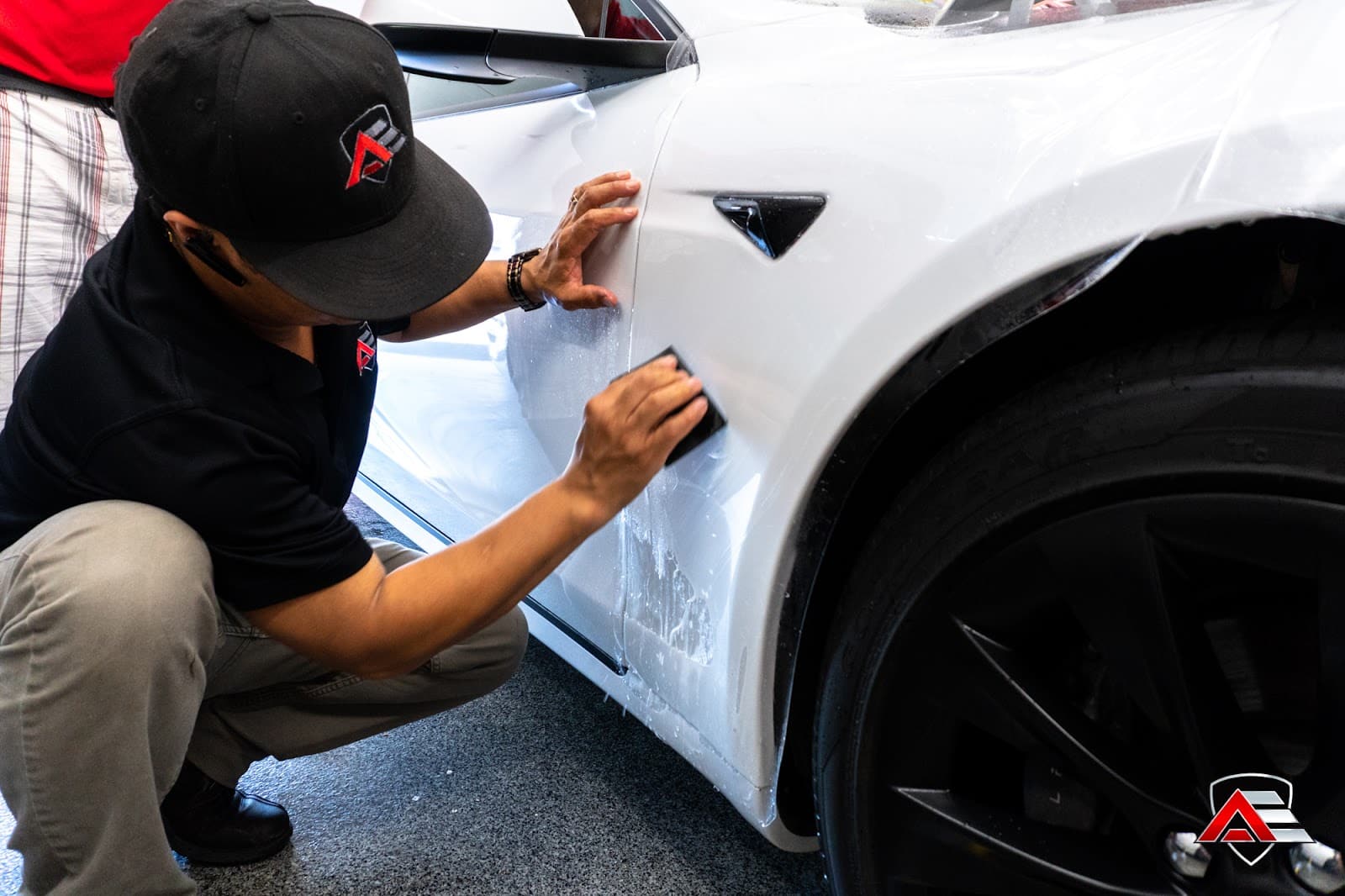 Person in a black cap and shirt applying protective film to the white side panel of a car.
