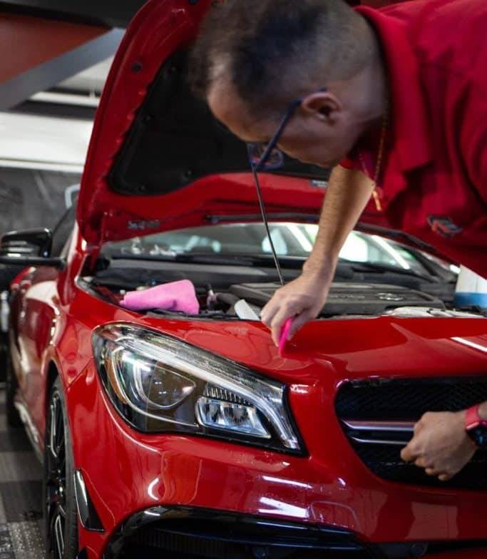 Man in red applying paint protection film to the hood of a shiny red car.