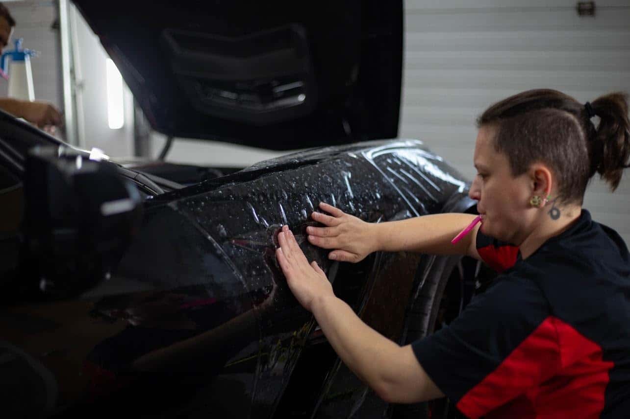 Technician applying protective film to the front fender of a black car.