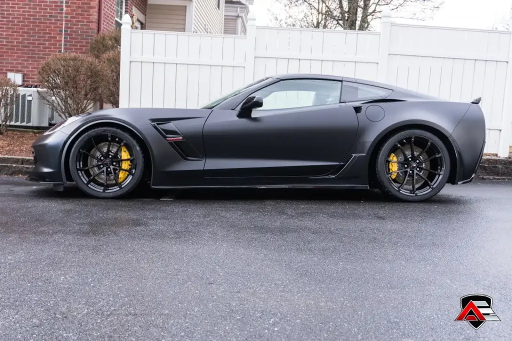 Side view of a matte black Corvette C7 Z06 on a wet street.