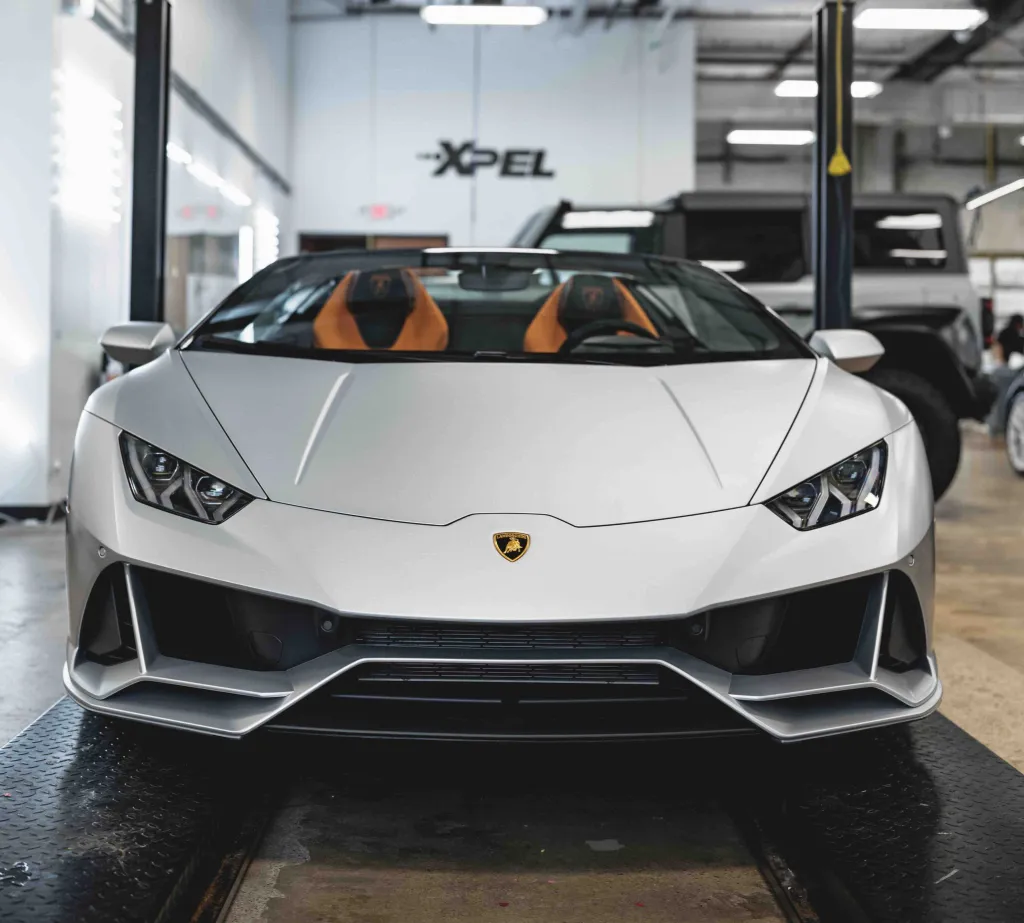 Front view of a white Lamborghini Huracan supercar with orange seats inside, on a garage lift.