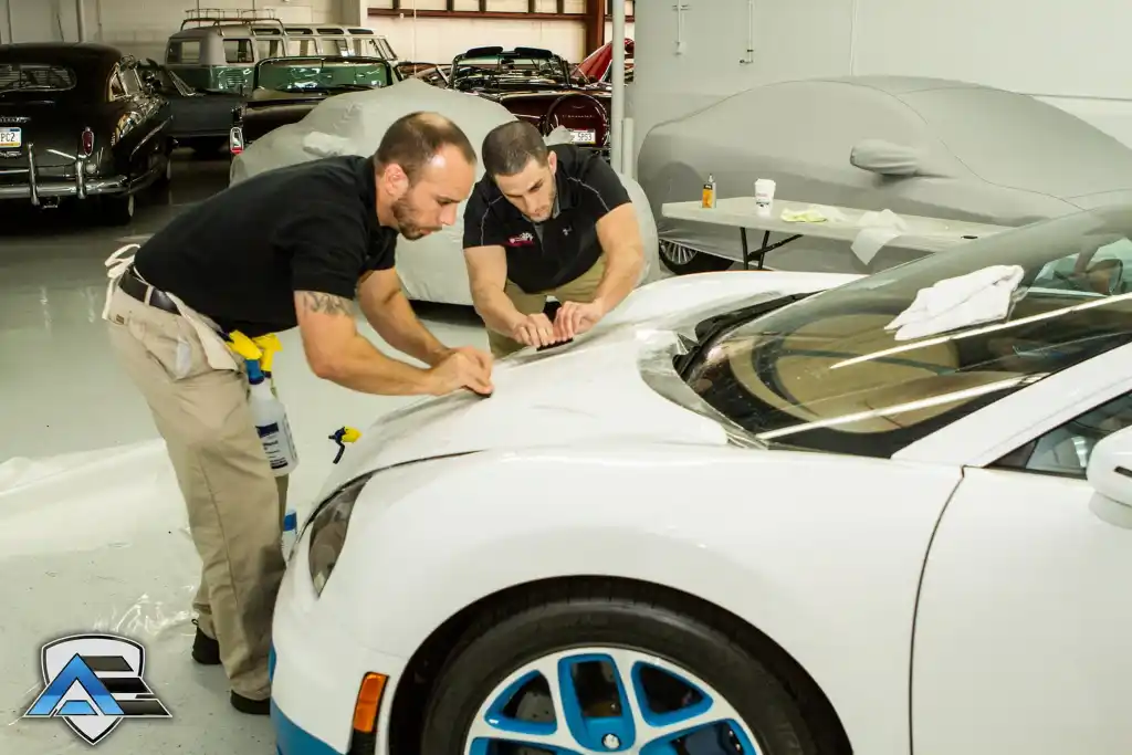 Technicians smoothing paint protection film across the hood of a Bugatti Veyron