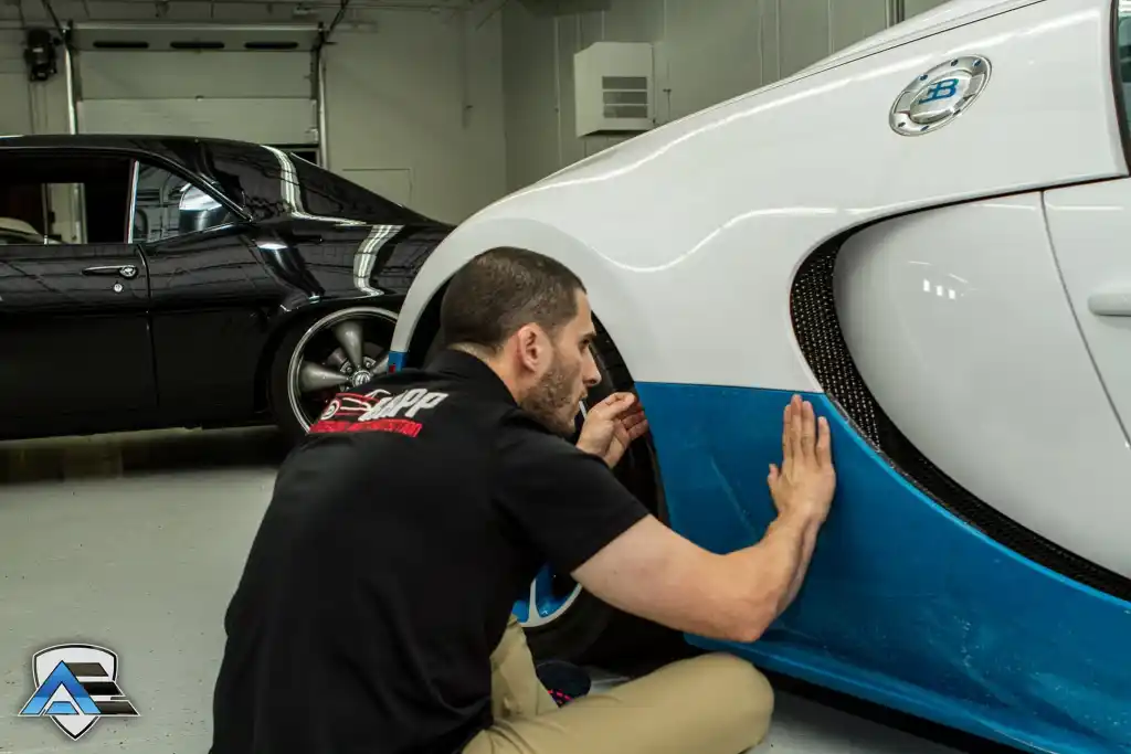 Technician smoothing paint protection film on the lower body panel of a Bugatti Veyron