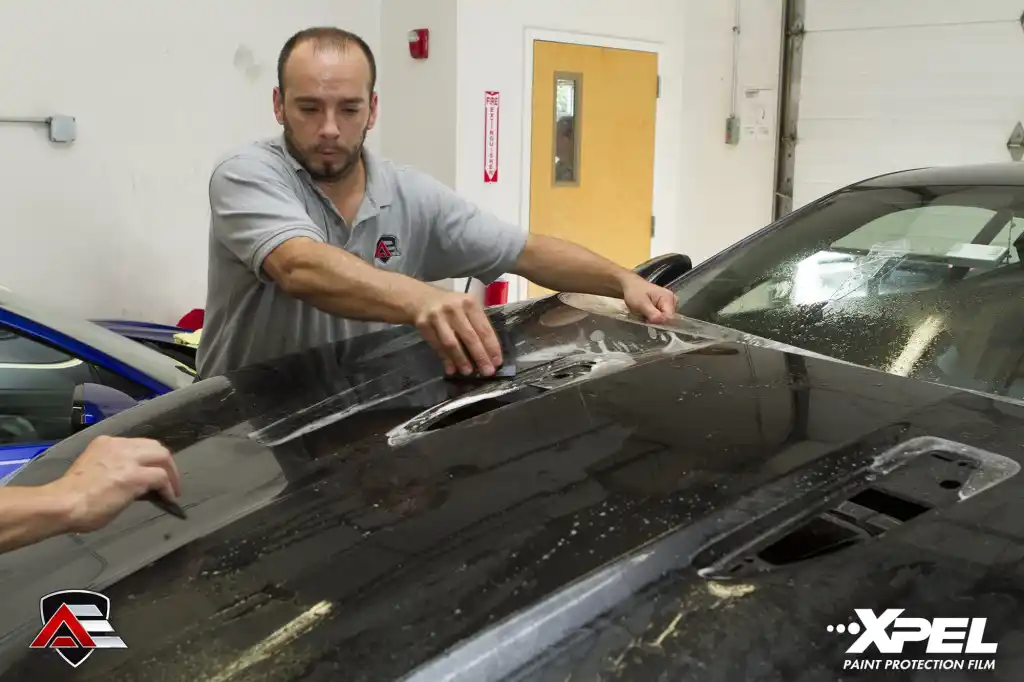 Technician applying XPEL paint protection film to the hood of a Jaguar F-TYPE R