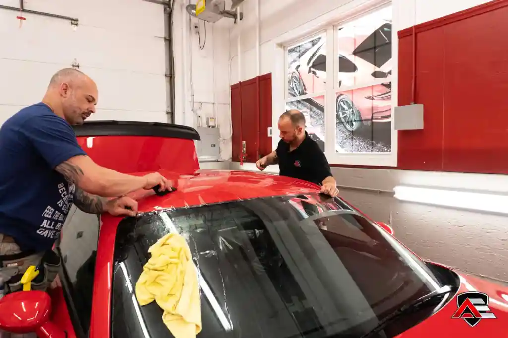 2Technicians smoothing paint protection film across the roof of a red Dodge Demon