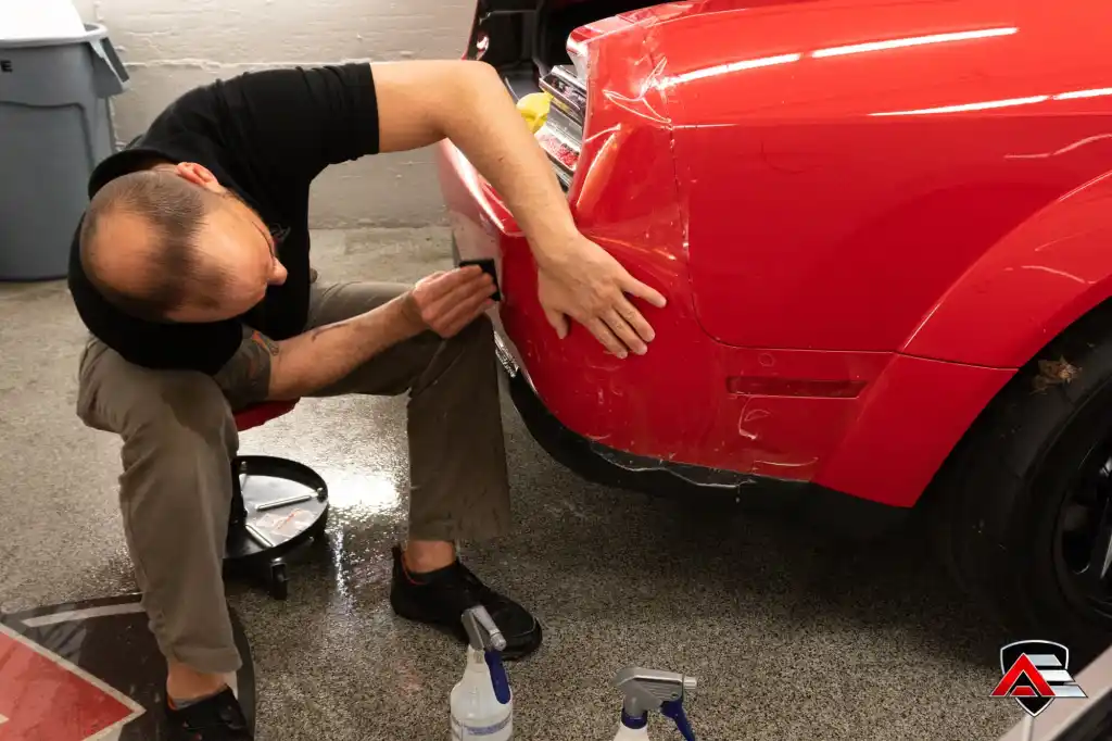 Technician applying paint protection film to the rear quarter panel of a red Dodge Demon