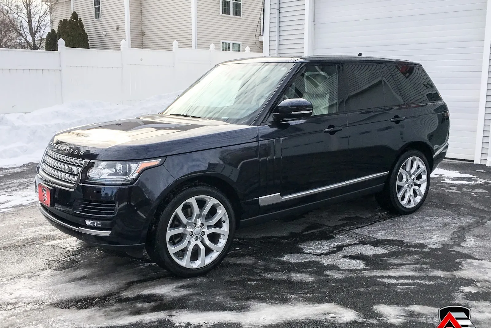 CDark blue Range Rover parked on a partially snow-covered driveway with a white fence and garage in the background.