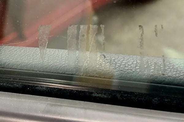 Streaks of dried residue on a car window, with a textured gray window sill beneath.
