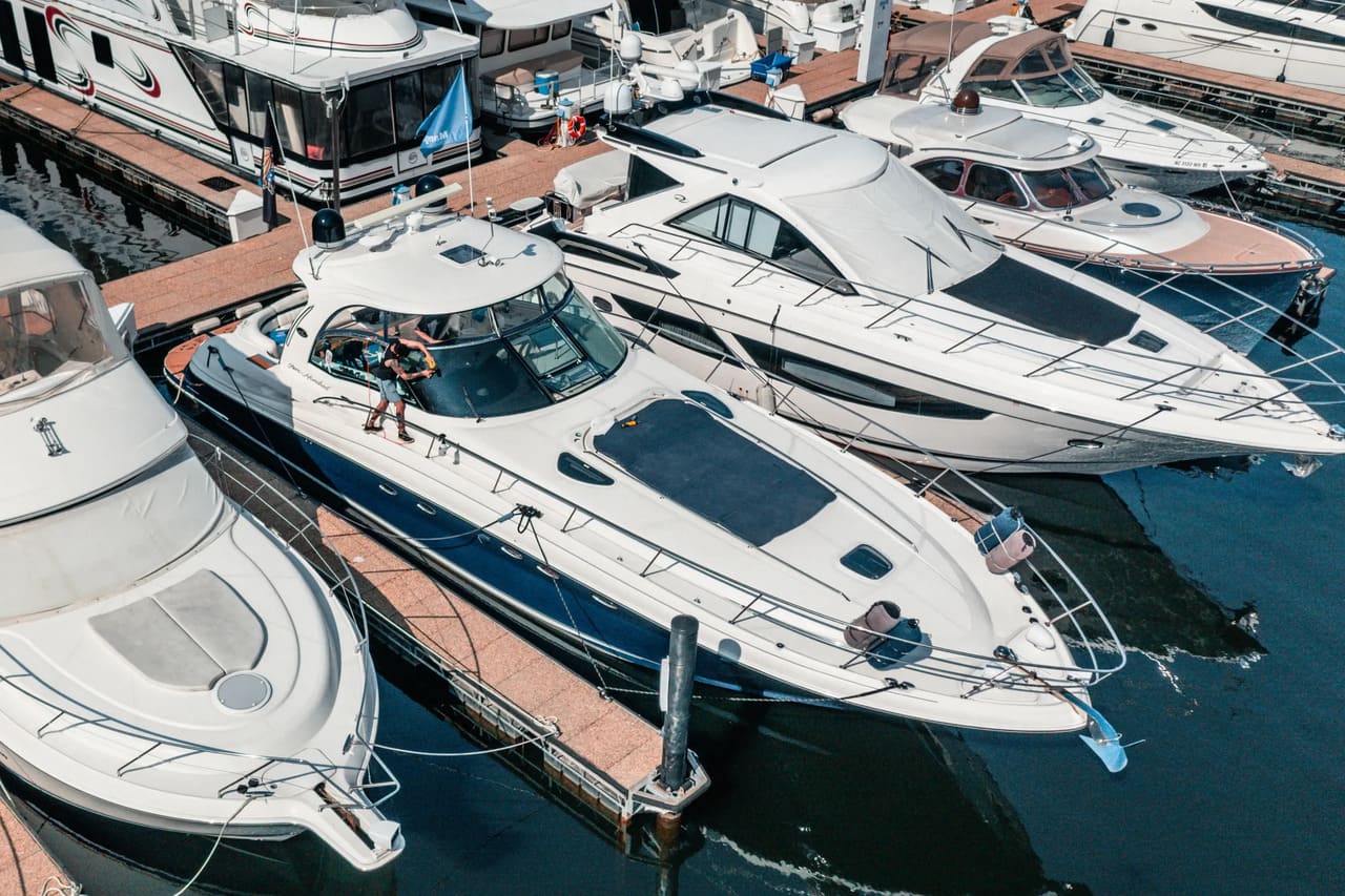 Aerial view of luxury yachts docked at a marina, with a person cleaning a blue and white boat.