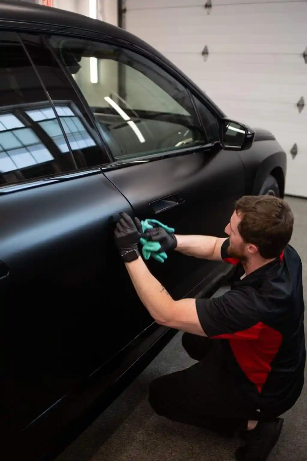 Technician cleaning matte paint protection film on a black SUV door