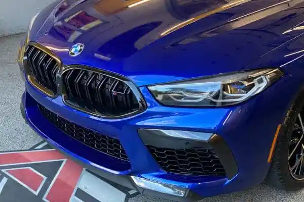 Front view of a shiny blue BMW M8 with its iconic kidney grilles, headlights, and lower grilles visible.