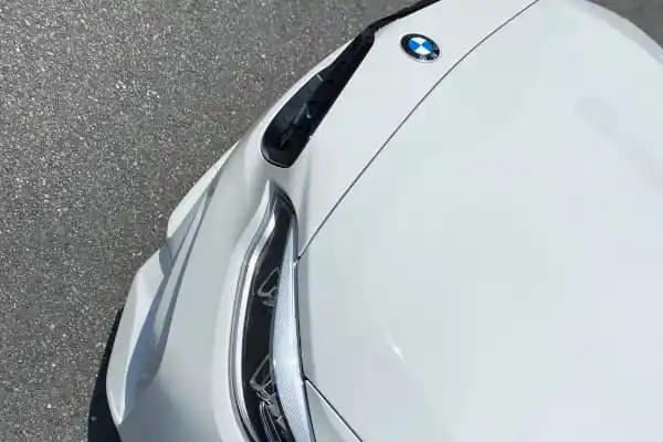 Overhead view of the front of a white BMW, showing the hood, headlight, and BMW logo.