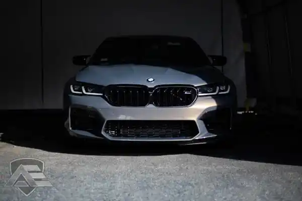 Front view of a dark gray BMW with headlights on, illuminated from above against a dark background.