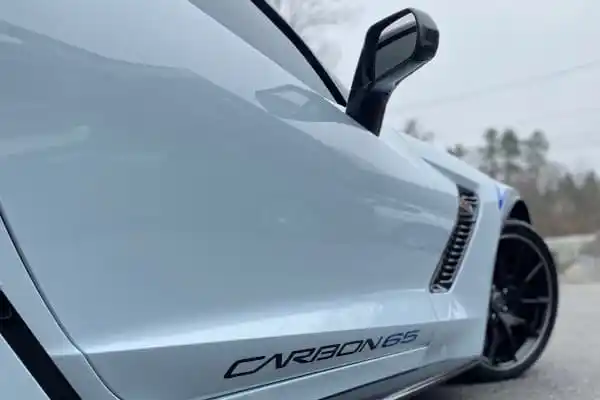Side view of a white Chevrolet Corvette with CARBON 65 written on the side, parked on an asphalt road.