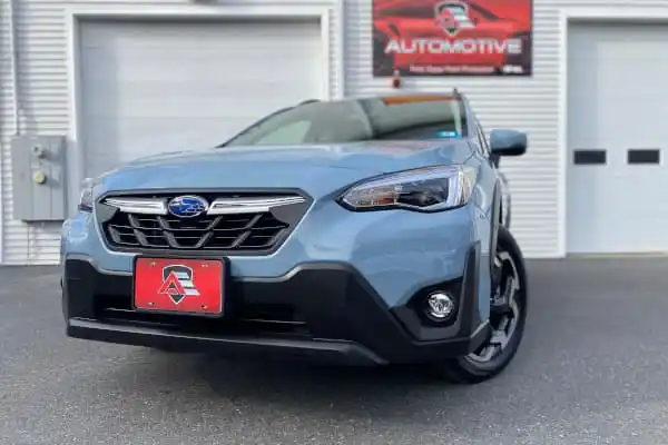 Front view of a light blue Subaru Crosstrek parked in front of a white building with an Automotive sign.