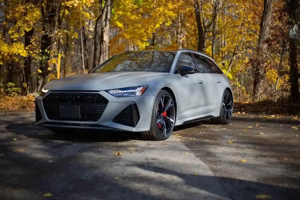 Gray Audi RS 6 Avant parked on an asphalt road with yellow and orange fall foliage in the background.