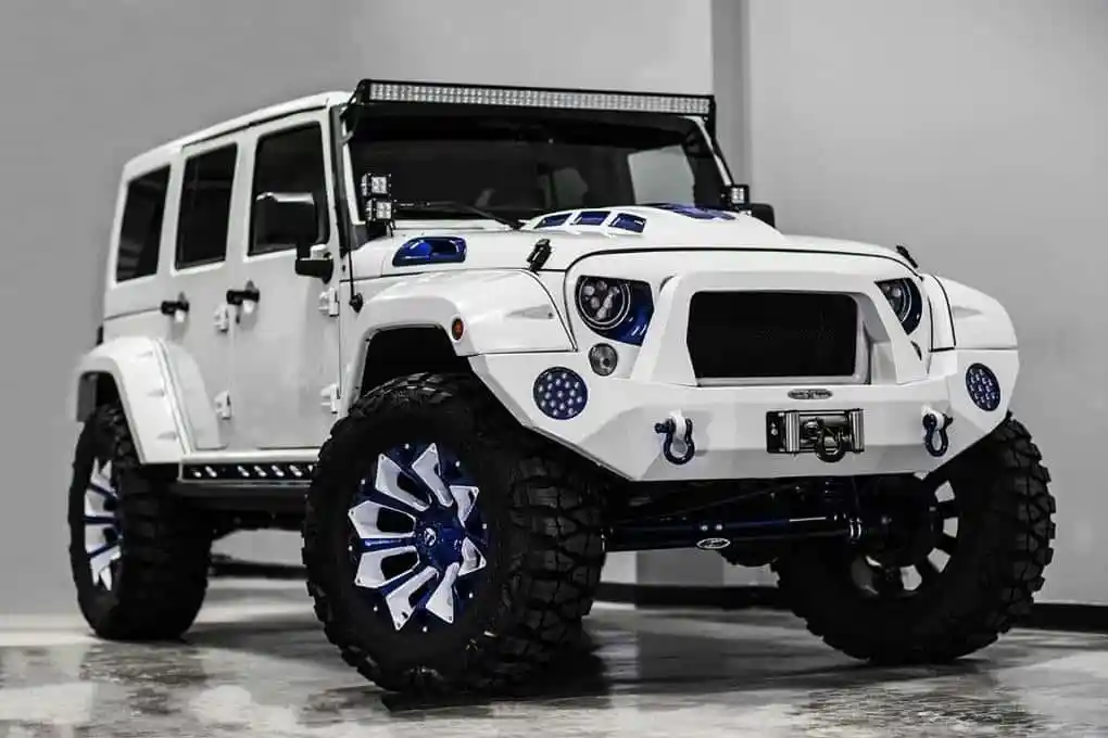 Customized white Jeep Wrangler with blue accents, large off-road tires, and a front winch, angled right.
