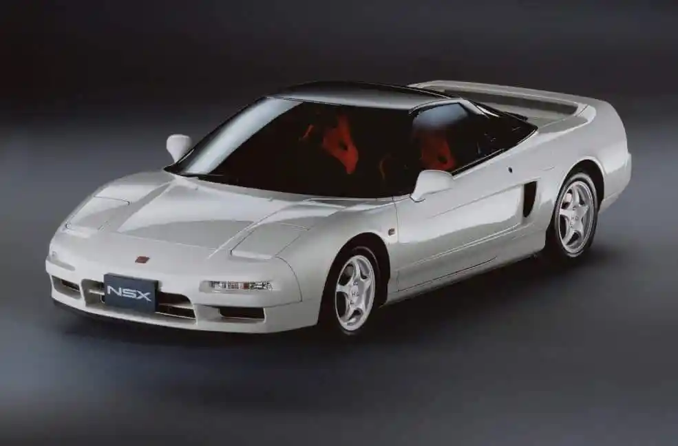 A white 1990s Honda NSX sports car, with a black roof and red interior, seen from the front three-quarter view.
