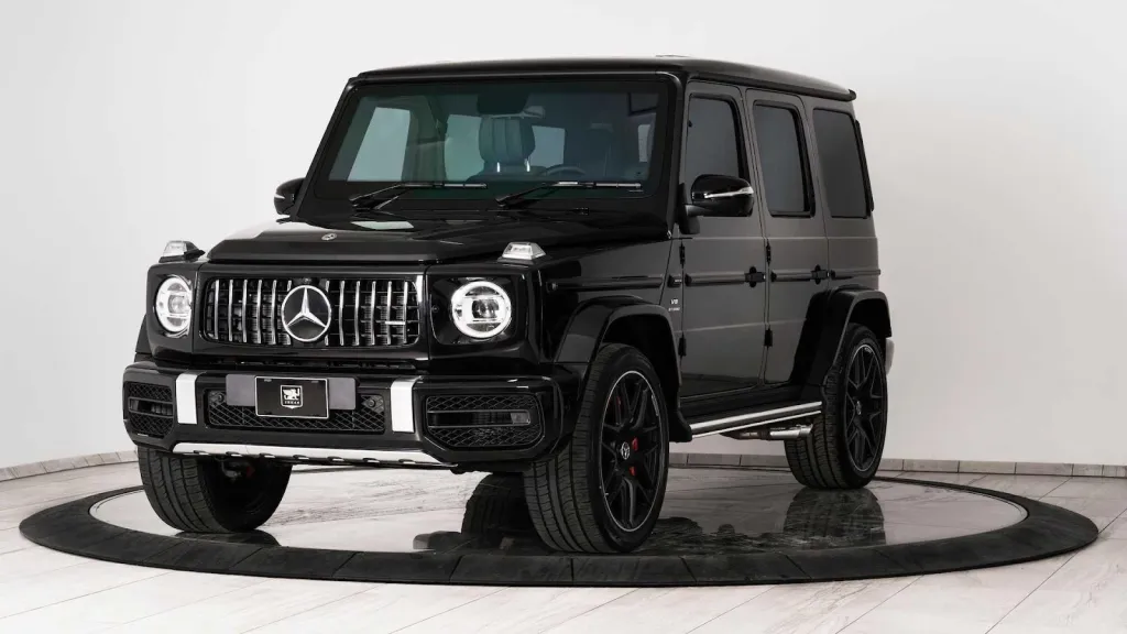 Front three-quarter view of a black Mercedes-Benz G-Wagen SUV with chrome grille, parked on a rotating platform.