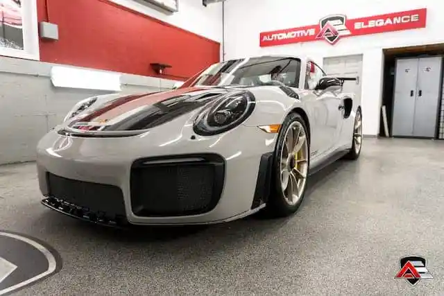 Front view of a light gray Porsche sportscar with black and red racing stripes parked in a garage.