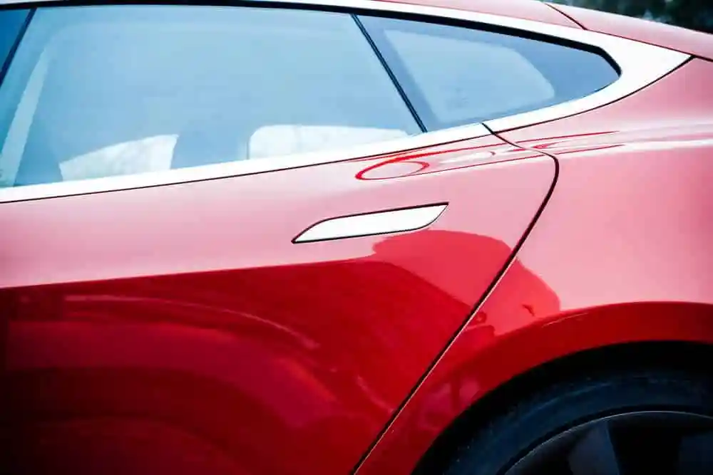 A shiny red Tesla with recessed door handles, a black tire, and light blue window tint, from the side.