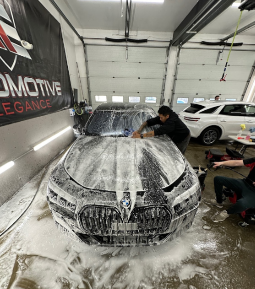 Person washing a black BMW covered in white foam inside a garage.
